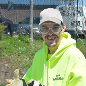 A man with safety yellow sweatshirt and baseball cap on the job working for HMEA's lawn care business