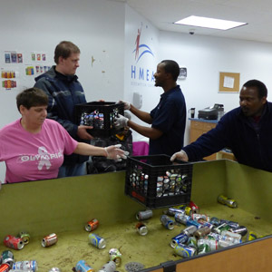 a woman and 2 men with an HMEA staff person working in HMEA's redemption center sorting cans