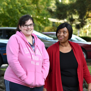 shared living - white woman in a pink sweatshirt and a woman of color in a red and black shirt going for walk
