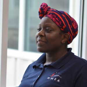 Woman of color wearing a red head wrap and an blue HMEA polo shirt