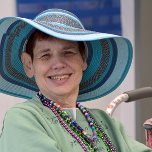 Woman in a sun hat, green shirt, and strings of beads who is served by HMEA