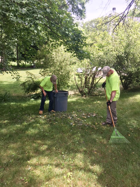 2 men wearing safety yellow t-shirt raking leaves for HMEA's lawn care buisness