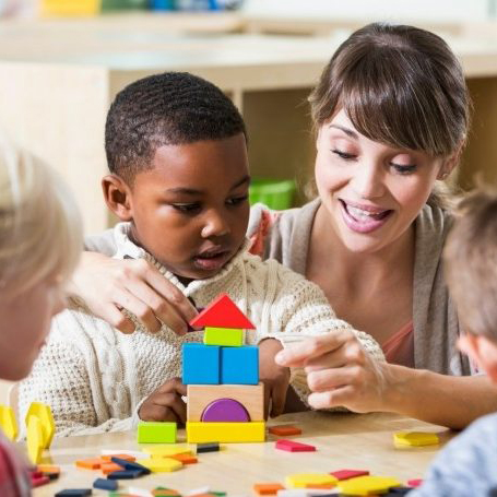 young boy playing with blocks being assisted by an female HMEA staff person